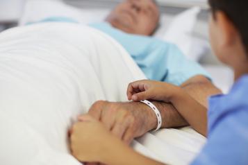 Nurse holding the hands of an elderly male patient lying on a hospital bed