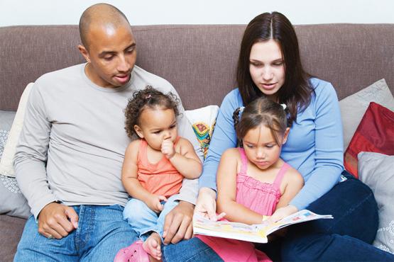 Black adult male and white adult female reading with their children