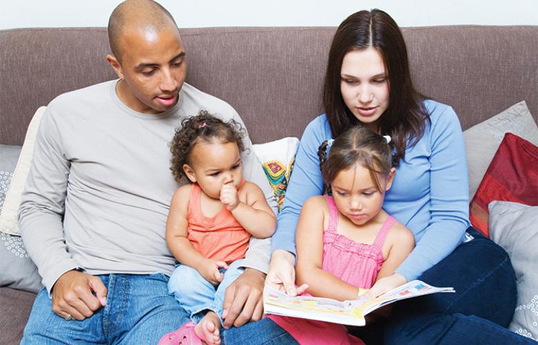 Black adult male and white adult female reading with their children